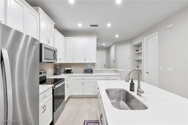 kitchen with light stone countertops, white cabinetry, stainless steel appliances, sink, and backsplash