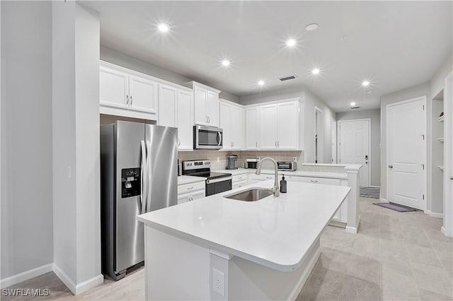 kitchen with white cabinetry, stainless steel appliances, decorative backsplash, sink, and a center island with sink