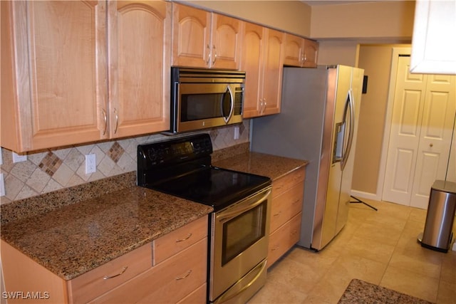 kitchen with light brown cabinetry, light tile patterned floors, decorative backsplash, appliances with stainless steel finishes, and dark stone countertops