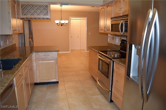 kitchen featuring stainless steel appliances, decorative light fixtures, light brown cabinetry, dark stone counters, and a notable chandelier