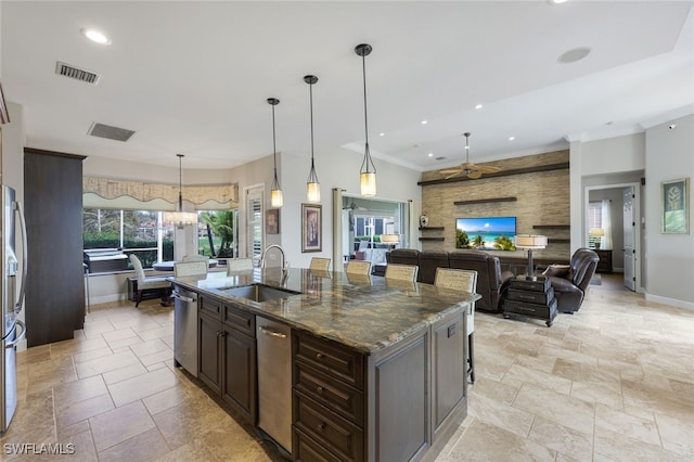 kitchen featuring dark stone counters, a center island with sink, hanging light fixtures, sink, and ceiling fan