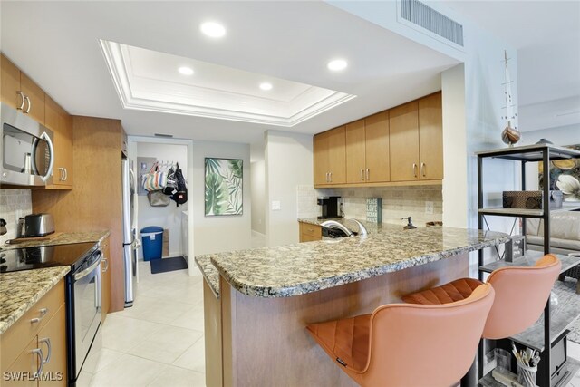 kitchen featuring stainless steel appliances, a kitchen breakfast bar, tasteful backsplash, a tray ceiling, and kitchen peninsula