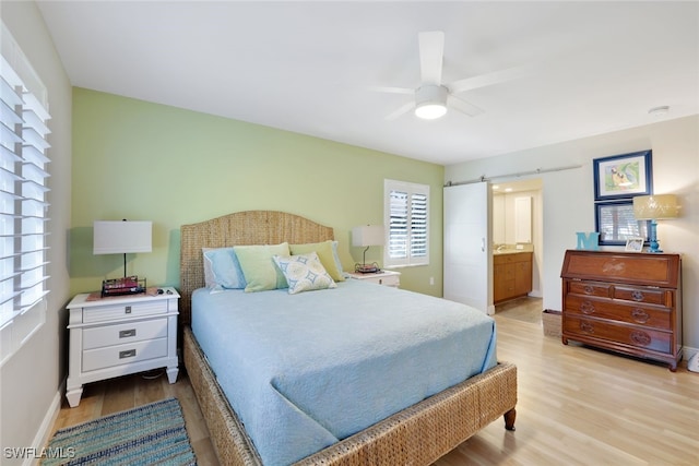 bedroom featuring ceiling fan, ensuite bathroom, a barn door, and light hardwood / wood-style flooring