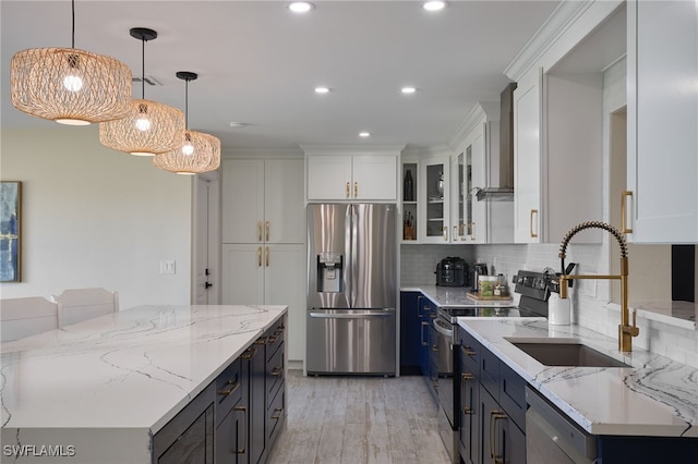 kitchen with pendant lighting, sink, white cabinets, stainless steel appliances, and wall chimney range hood