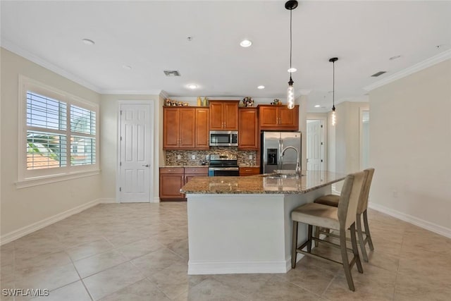 kitchen featuring stone counters, hanging light fixtures, stainless steel appliances, backsplash, and an island with sink