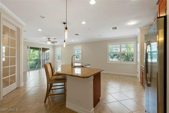 kitchen featuring sink, light stone counters, stainless steel fridge, decorative light fixtures, and ornamental molding