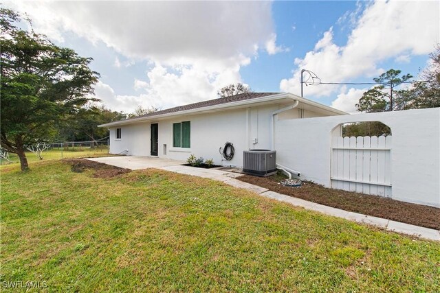 rear view of house with central AC unit, a patio area, and a lawn