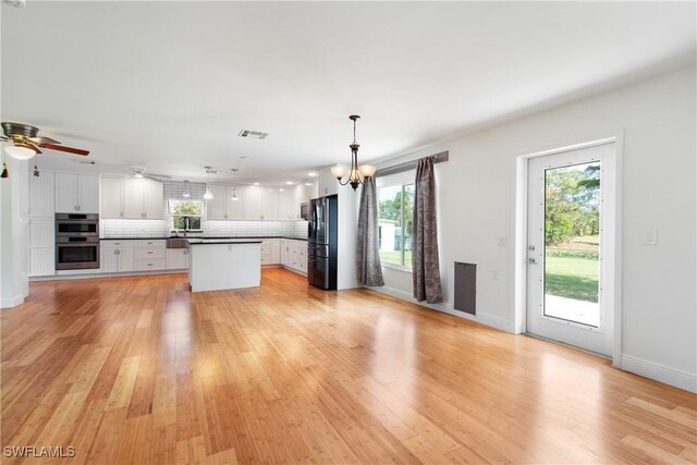 kitchen with white cabinetry, black fridge, backsplash, decorative light fixtures, and a kitchen island