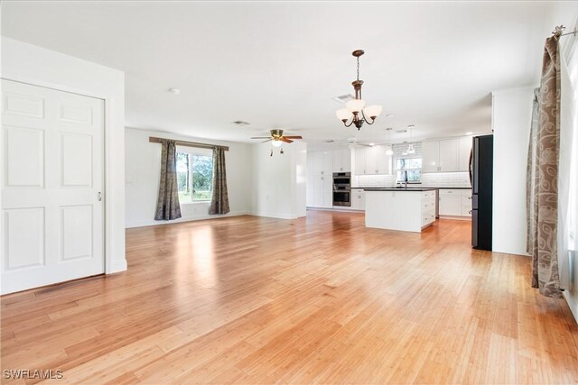 unfurnished living room featuring ceiling fan with notable chandelier and light wood-type flooring