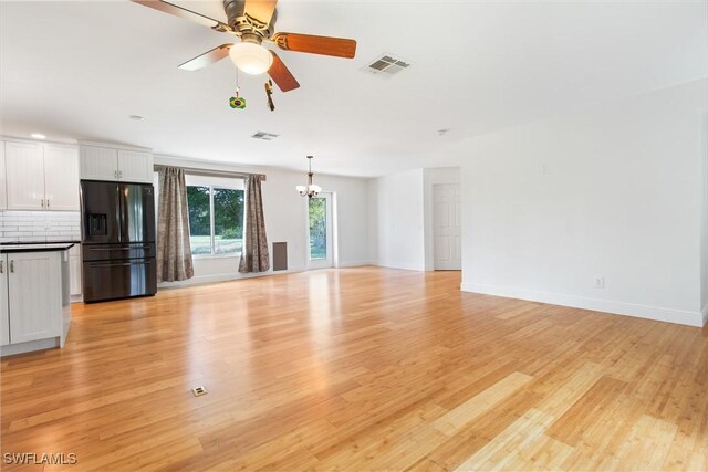 unfurnished living room featuring ceiling fan with notable chandelier and light wood-type flooring