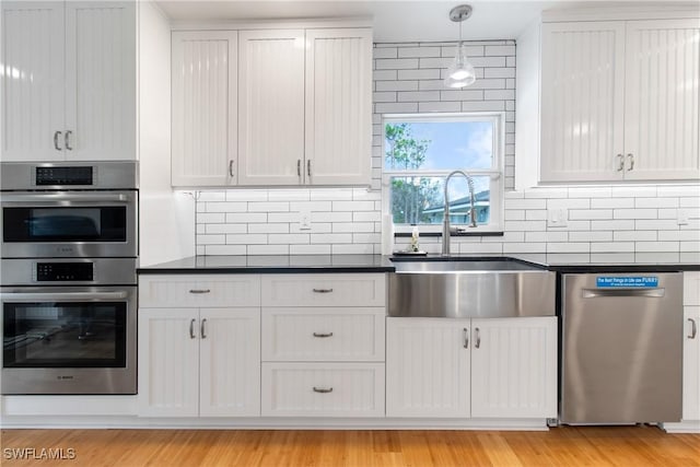 kitchen with appliances with stainless steel finishes, decorative light fixtures, white cabinetry, and sink