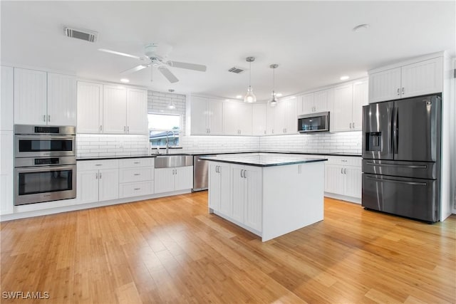 kitchen with a center island, white cabinets, stainless steel appliances, and decorative light fixtures