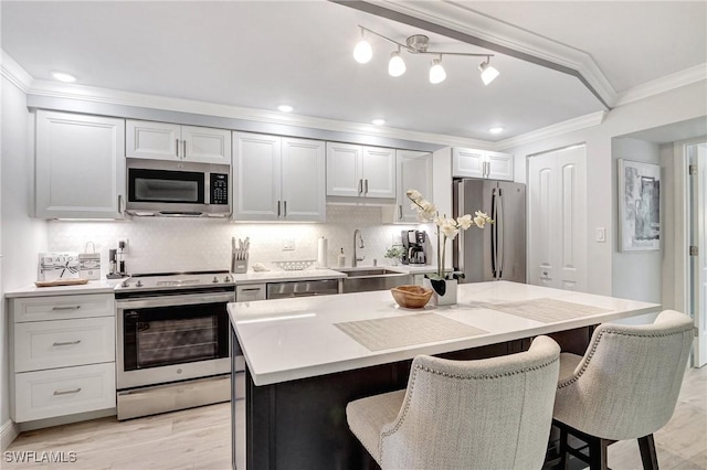 kitchen featuring a kitchen island, appliances with stainless steel finishes, sink, white cabinets, and a kitchen bar