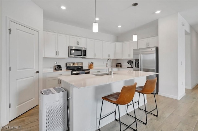 kitchen featuring appliances with stainless steel finishes, sink, white cabinets, hanging light fixtures, and a center island with sink