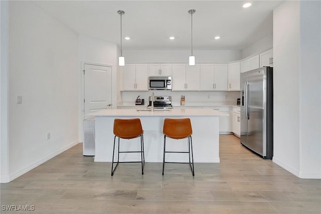 kitchen with decorative light fixtures, sink, white cabinets, stainless steel appliances, and a center island with sink