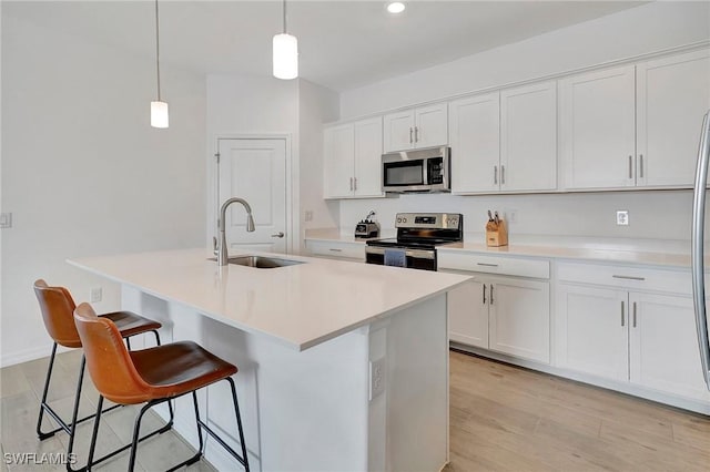 kitchen with stainless steel appliances, an island with sink, sink, and white cabinets