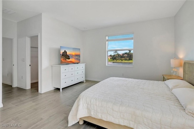 bedroom featuring a walk in closet, light hardwood / wood-style floors, and a closet