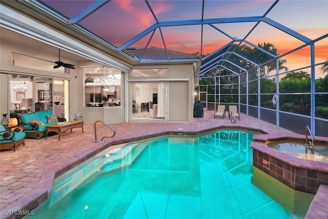 pool at dusk featuring an in ground hot tub, glass enclosure, ceiling fan, and a patio area