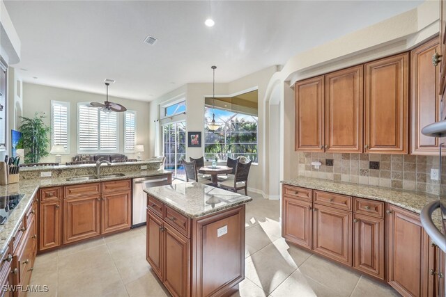 kitchen with stainless steel dishwasher, decorative light fixtures, light stone countertops, and sink