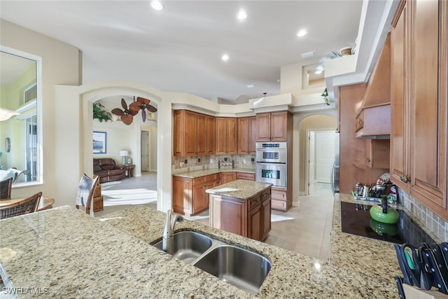 kitchen with a kitchen island, light stone countertops, sink, and double oven