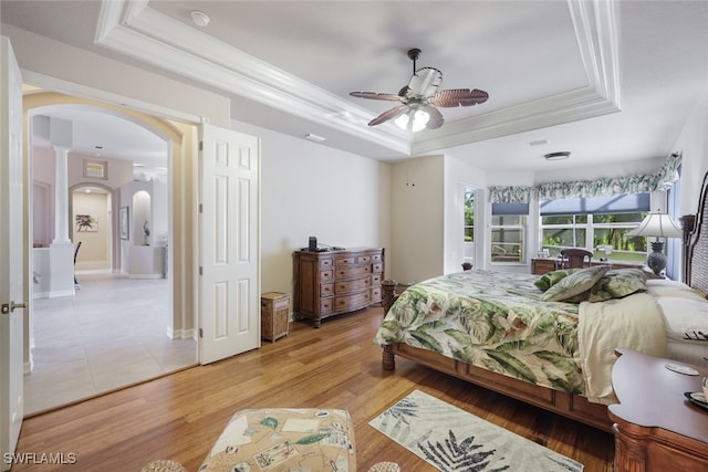 bedroom featuring ceiling fan, ornate columns, ornamental molding, a tray ceiling, and wood-type flooring