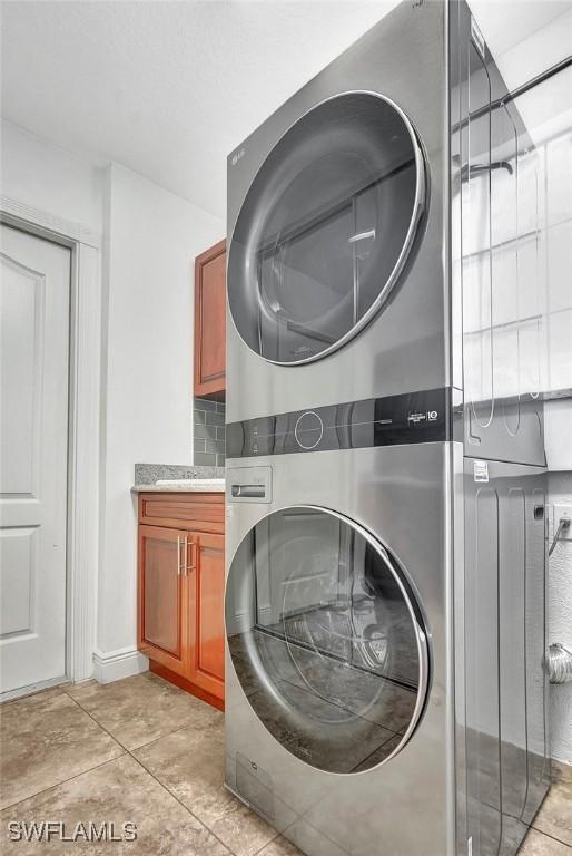 washroom featuring cabinets, light tile patterned floors, and stacked washer and clothes dryer