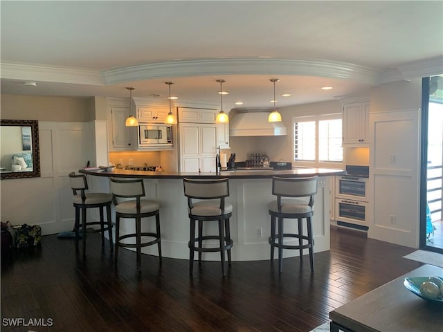 kitchen with a kitchen breakfast bar, stainless steel microwave, white cabinets, and decorative light fixtures