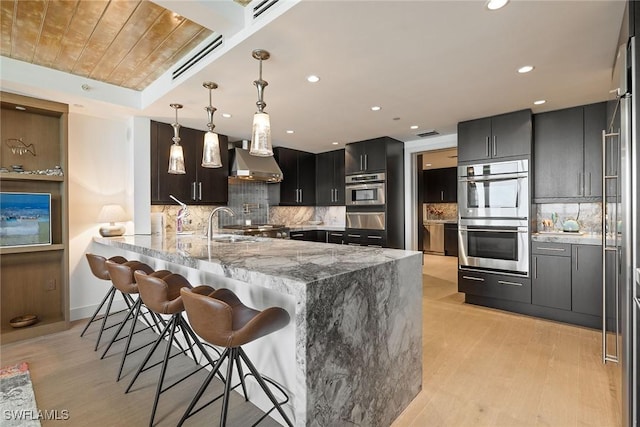 kitchen with wall chimney range hood, pendant lighting, kitchen peninsula, a kitchen breakfast bar, and double oven