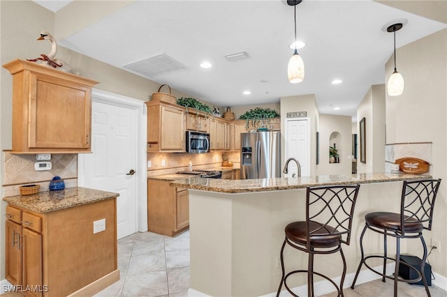 kitchen featuring kitchen peninsula, appliances with stainless steel finishes, decorative light fixtures, and light stone counters