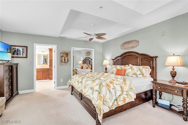 bedroom with ensuite bathroom, ceiling fan, light colored carpet, and a tray ceiling