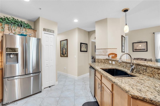 kitchen with light brown cabinets, sink, hanging light fixtures, light stone countertops, and stainless steel appliances