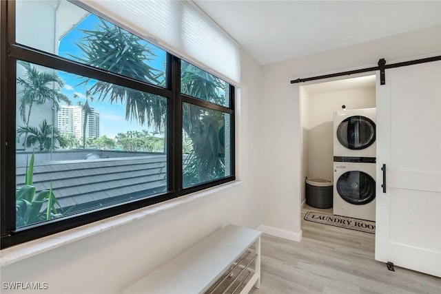 laundry area featuring a barn door, stacked washer and dryer, and light hardwood / wood-style flooring