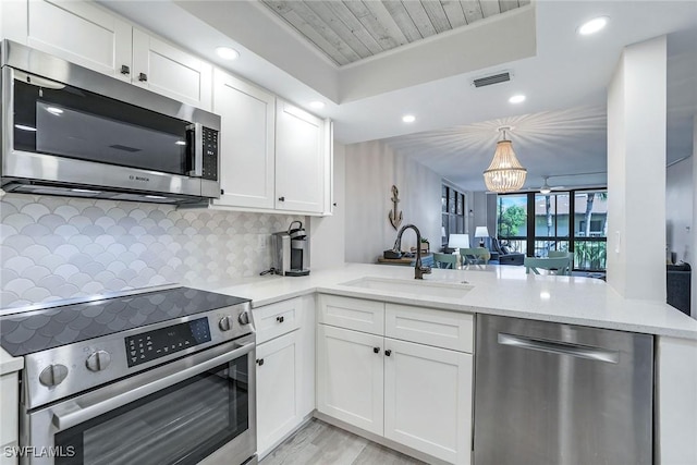 kitchen featuring kitchen peninsula, stainless steel appliances, sink, an inviting chandelier, and white cabinets