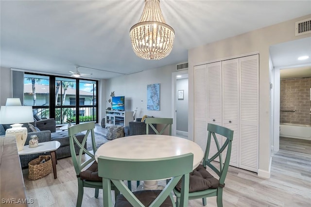 dining area with light wood-type flooring, ceiling fan with notable chandelier, and floor to ceiling windows