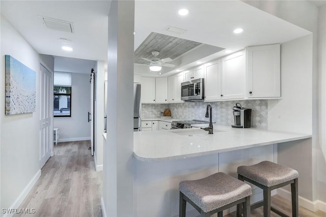 kitchen featuring kitchen peninsula, appliances with stainless steel finishes, a kitchen breakfast bar, sink, and white cabinetry