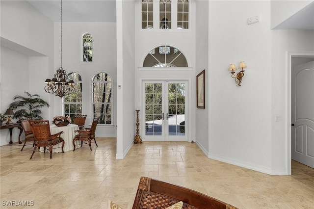 entrance foyer featuring a notable chandelier, a healthy amount of sunlight, a towering ceiling, and french doors