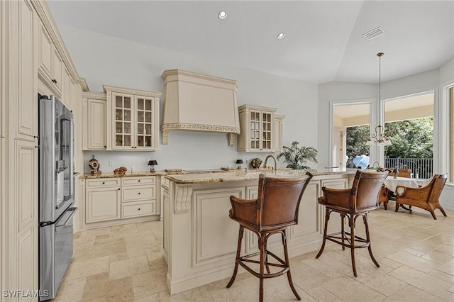 kitchen with cream cabinetry, custom range hood, hanging light fixtures, and stainless steel refrigerator