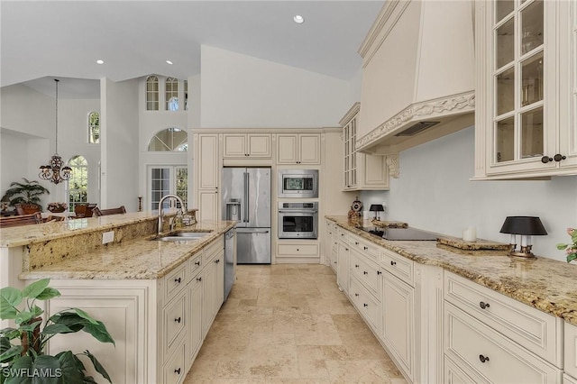 kitchen with light stone counters, stainless steel appliances, sink, cream cabinets, and hanging light fixtures