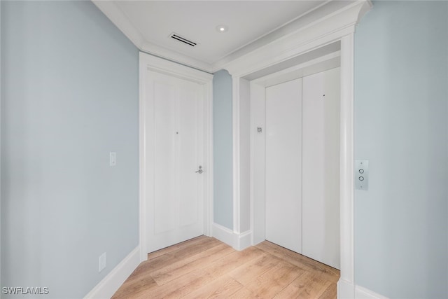 hallway with light hardwood / wood-style floors and ornamental molding