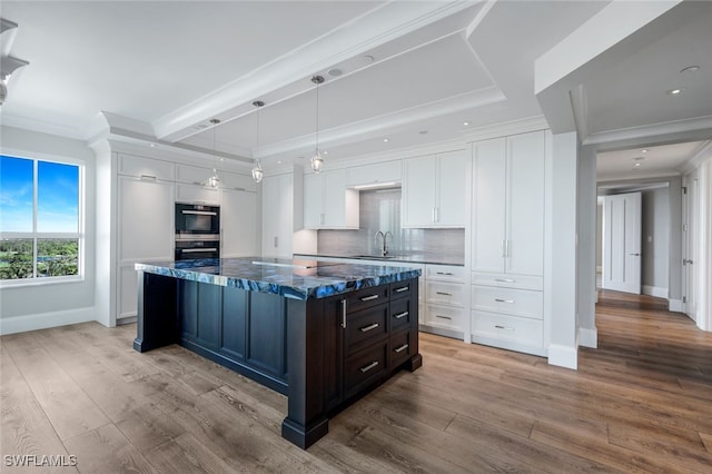 kitchen with light wood-type flooring, tasteful backsplash, sink, a center island, and white cabinetry