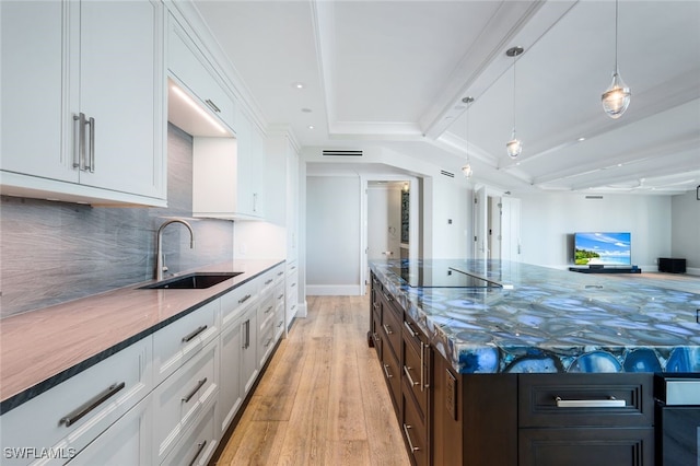 kitchen featuring white cabinetry, sink, hanging light fixtures, a tray ceiling, and light wood-type flooring