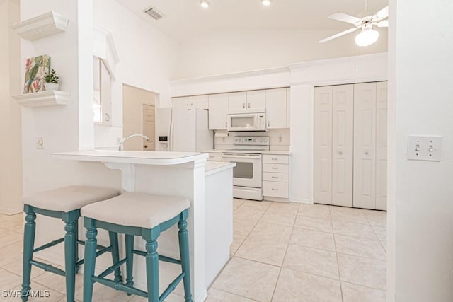 kitchen with white appliances, kitchen peninsula, a kitchen breakfast bar, and white cabinetry