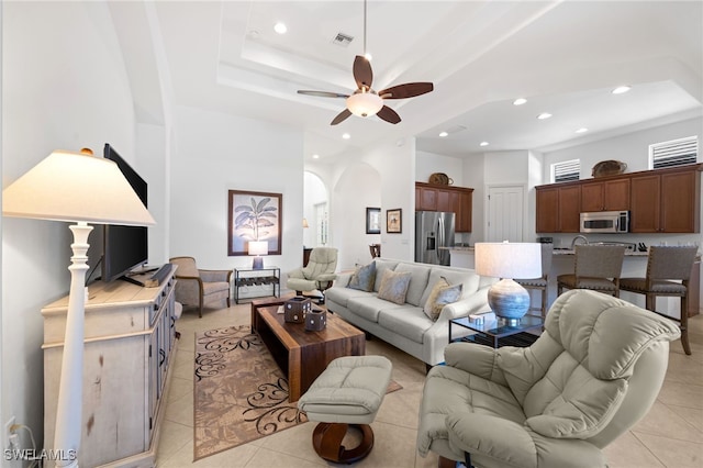 living room with a raised ceiling, ceiling fan, and light tile patterned flooring