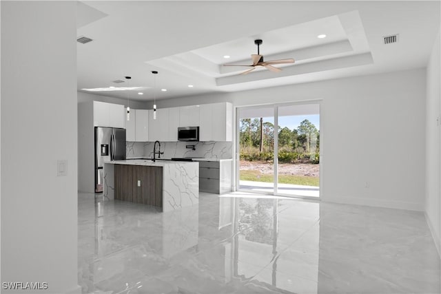 kitchen featuring hanging light fixtures, a raised ceiling, a kitchen island with sink, white cabinets, and appliances with stainless steel finishes