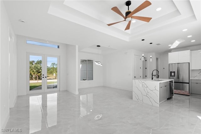 kitchen with a raised ceiling, white cabinets, an island with sink, and stainless steel appliances