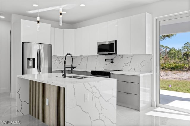 kitchen featuring stainless steel appliances, sink, pendant lighting, white cabinets, and an island with sink