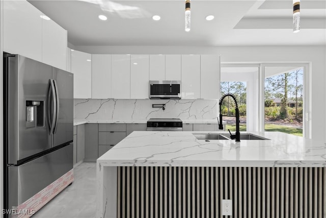 kitchen featuring light stone counters, stainless steel appliances, sink, white cabinetry, and hanging light fixtures