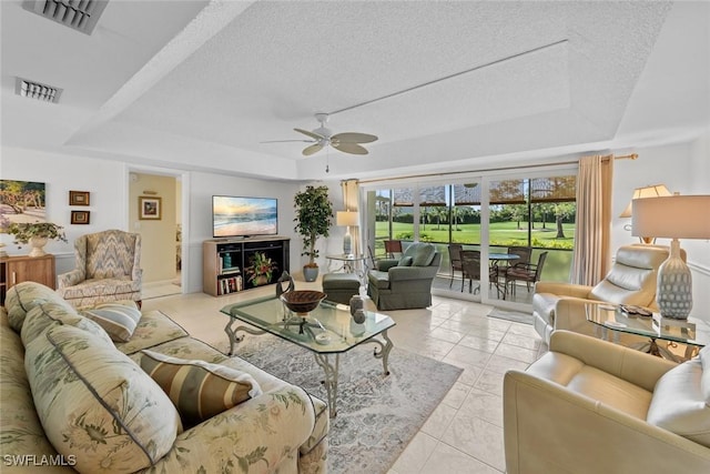 living room featuring a raised ceiling, ceiling fan, light tile patterned floors, and a textured ceiling