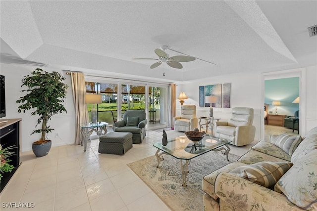 living room with a tray ceiling, ceiling fan, light tile patterned floors, and a textured ceiling