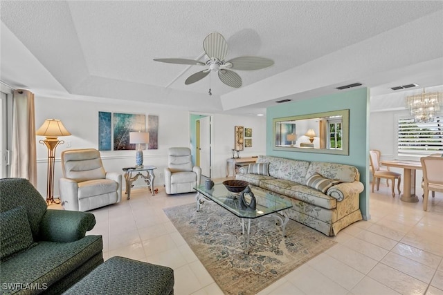 living room with ceiling fan with notable chandelier, light tile patterned flooring, a textured ceiling, and a tray ceiling